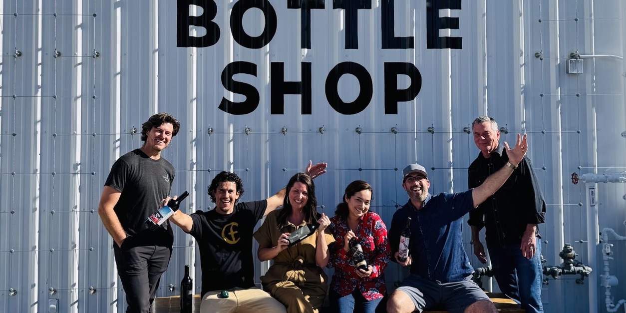 Six Bottle Shop makers gathered in front of the Bottle Shop sign